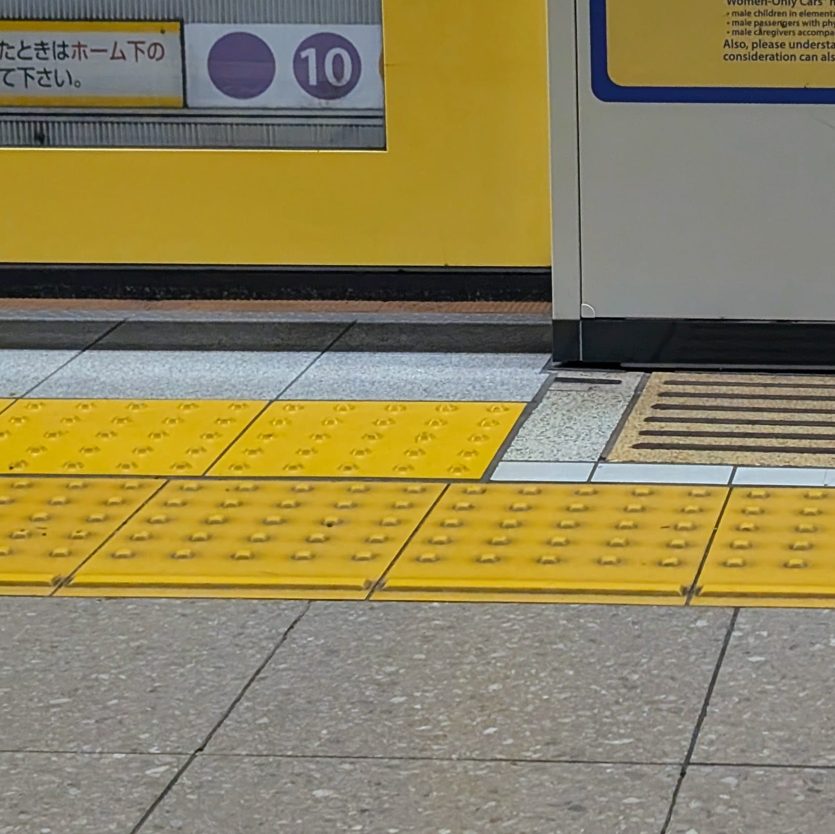 Braille blocks on the floor of a Japanese subway station, showing a grid of raised bumps and some lines, to indicate where to get on the train