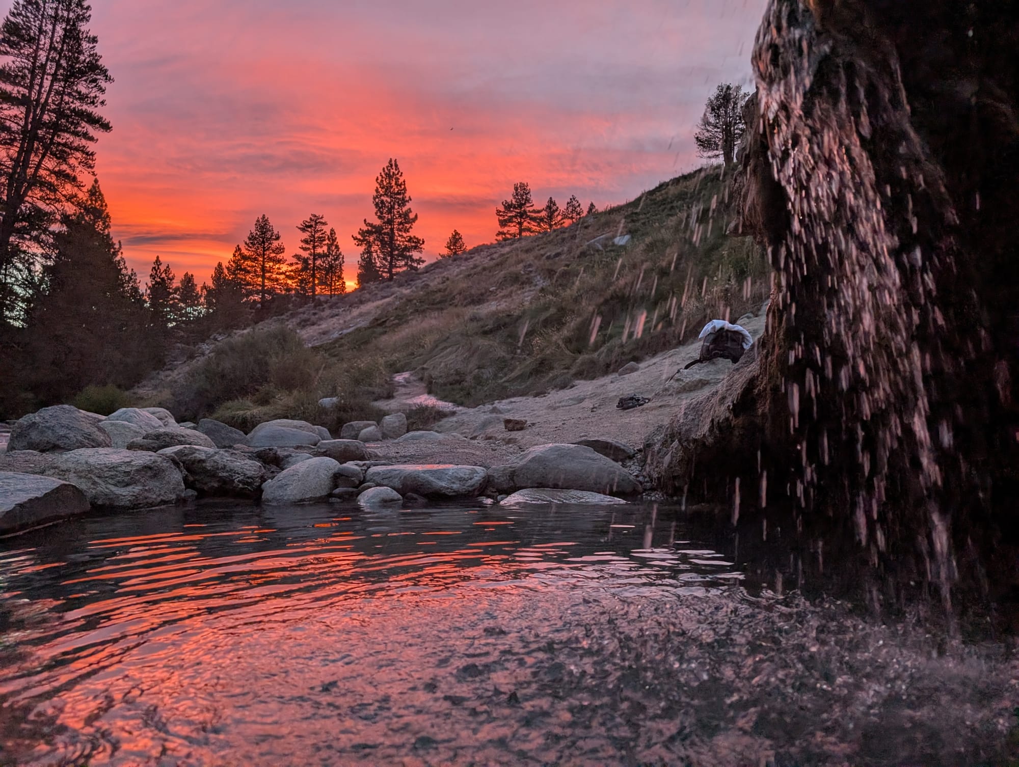 reds and purples in a sunset sky reflecting on a rock pool with a shower-like waterfall of water