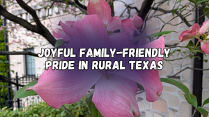 Joyful family-friendly Pride in rural Texas, with a close up of a pink flower on a bare tree branch with a stone wall